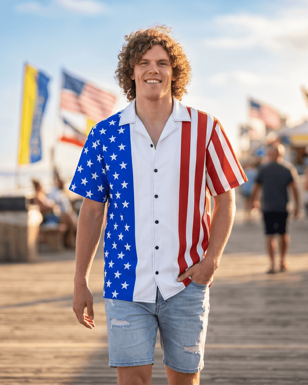 Man wearing an American flag shirt on a boardwalk with ocean and flags in the background