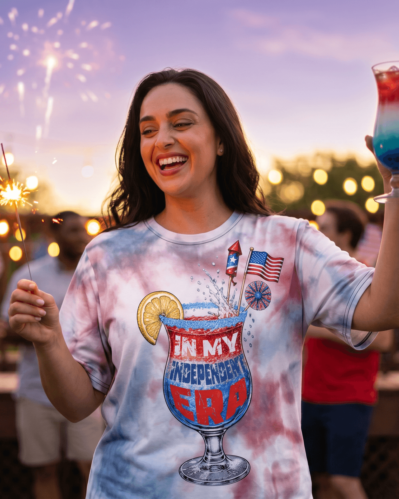 Woman in patriotic tie-dye tee with 'In My Independent Era' cocktail graphic, celebrating with sparklers and fireworks