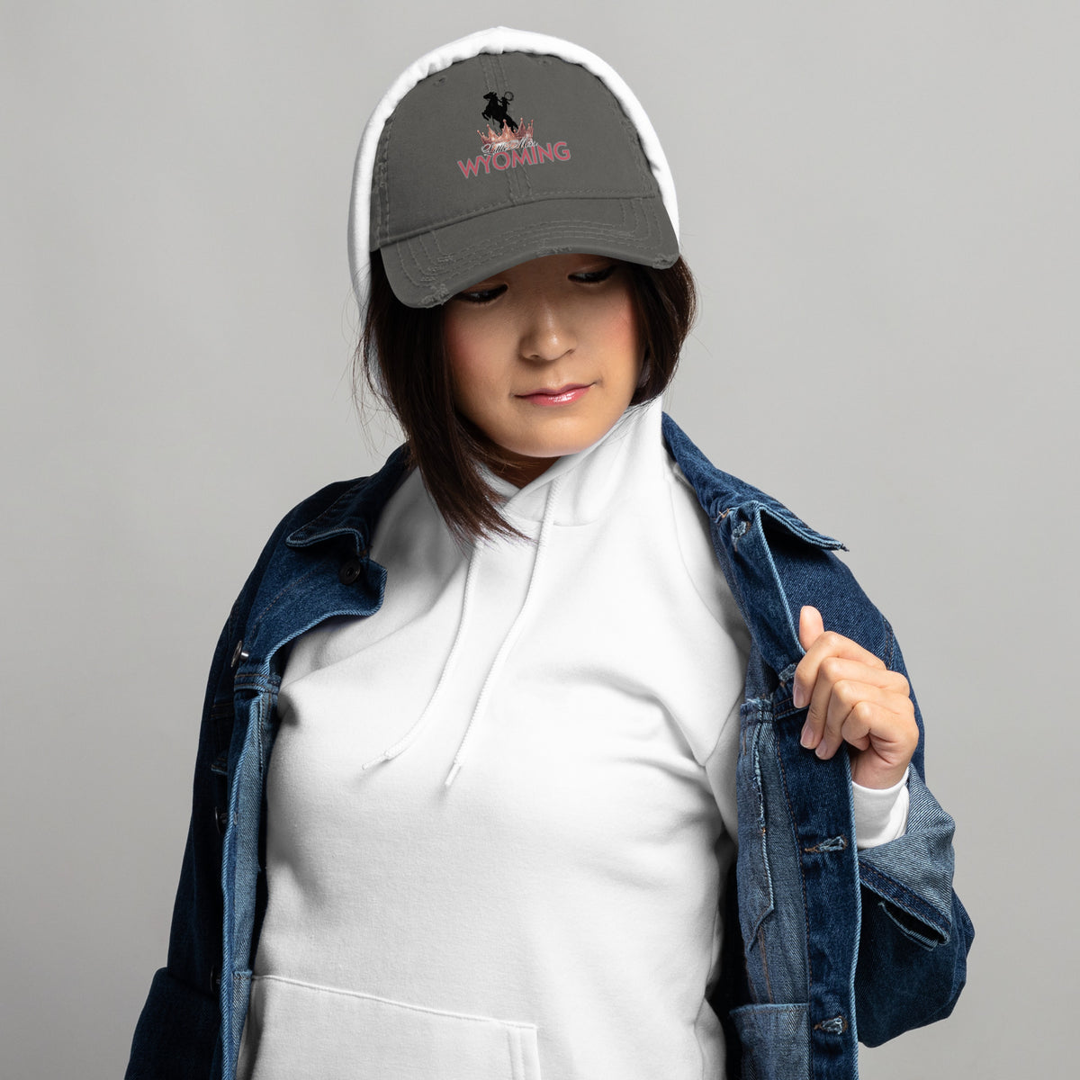 Person wearing a gray cap with a logo, white hoodie, and denim jacket on a gray background