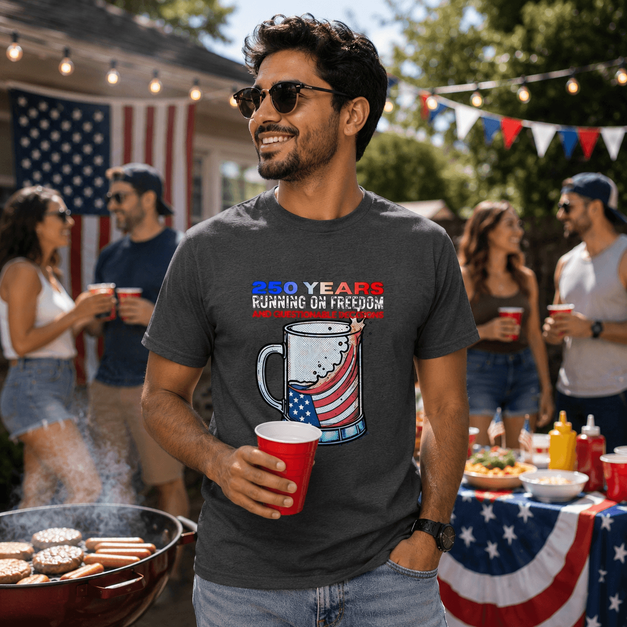 Man wearing patriotic graphic tee with '250 Years Running on Freedom' design at backyard BBQ, holding red cup