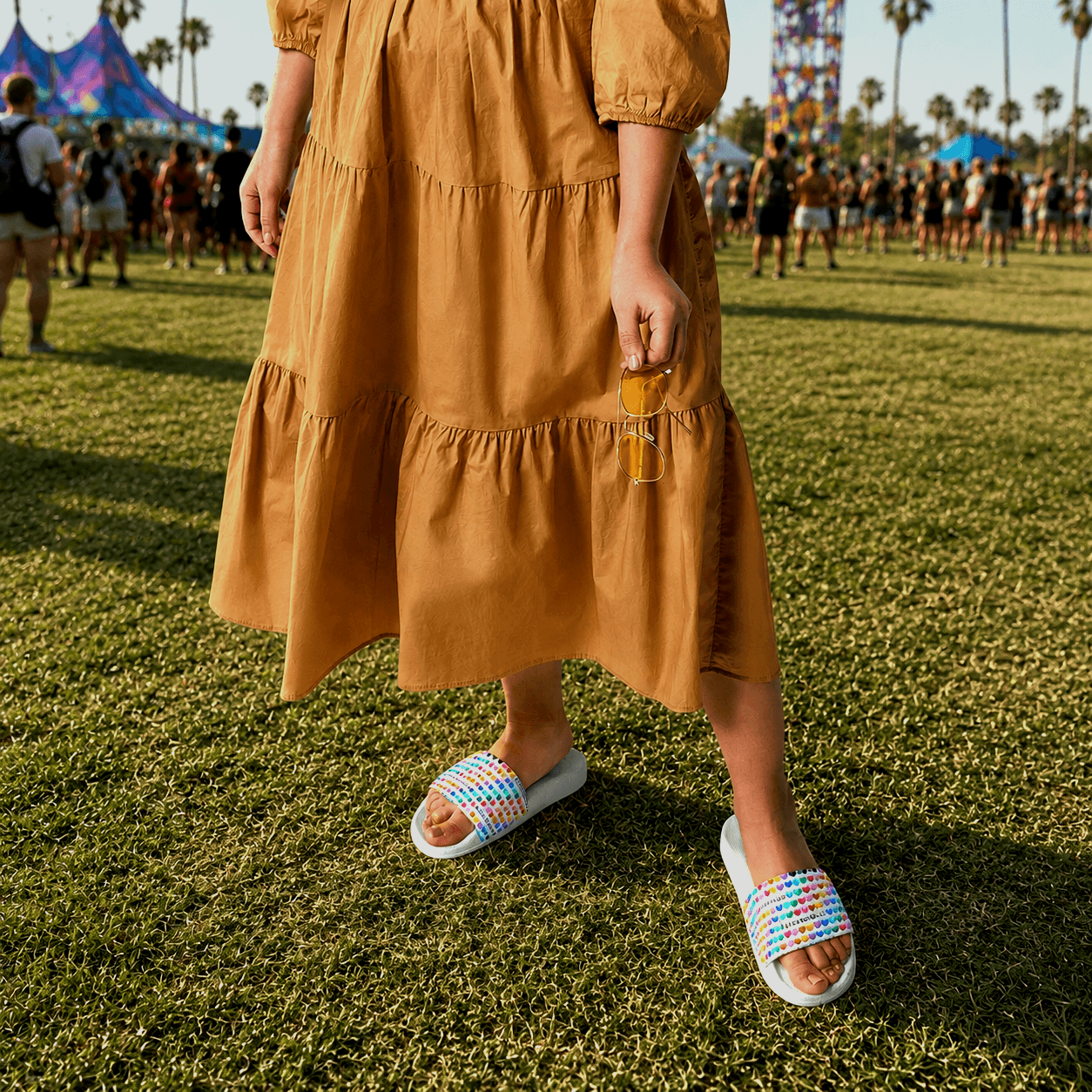 Colorful heart-patterned slide sandals worn at outdoor festival with palm trees and tents