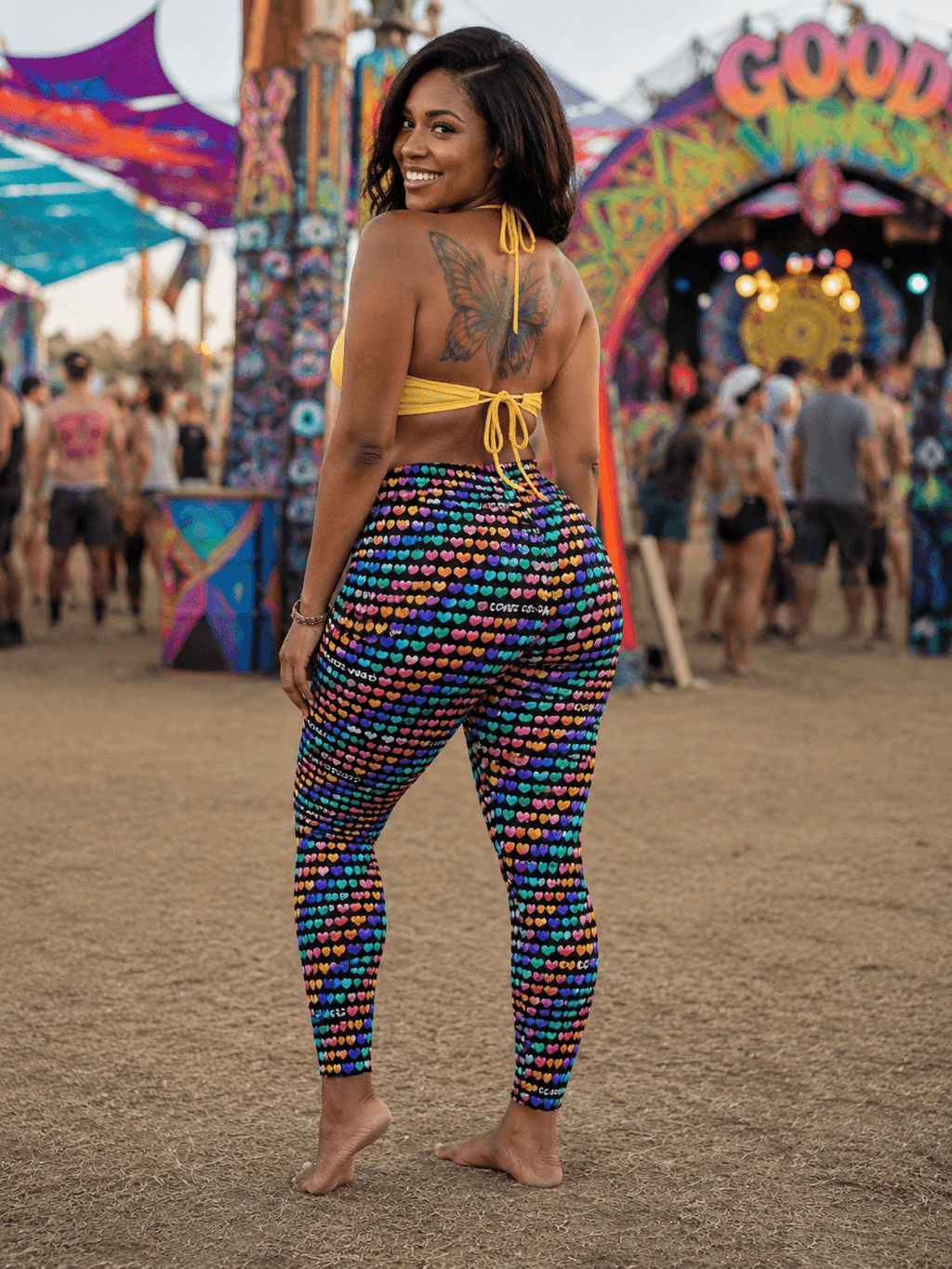 Woman in colorful heart-print leggings at vibrant festival, back view with butterfly tattoo