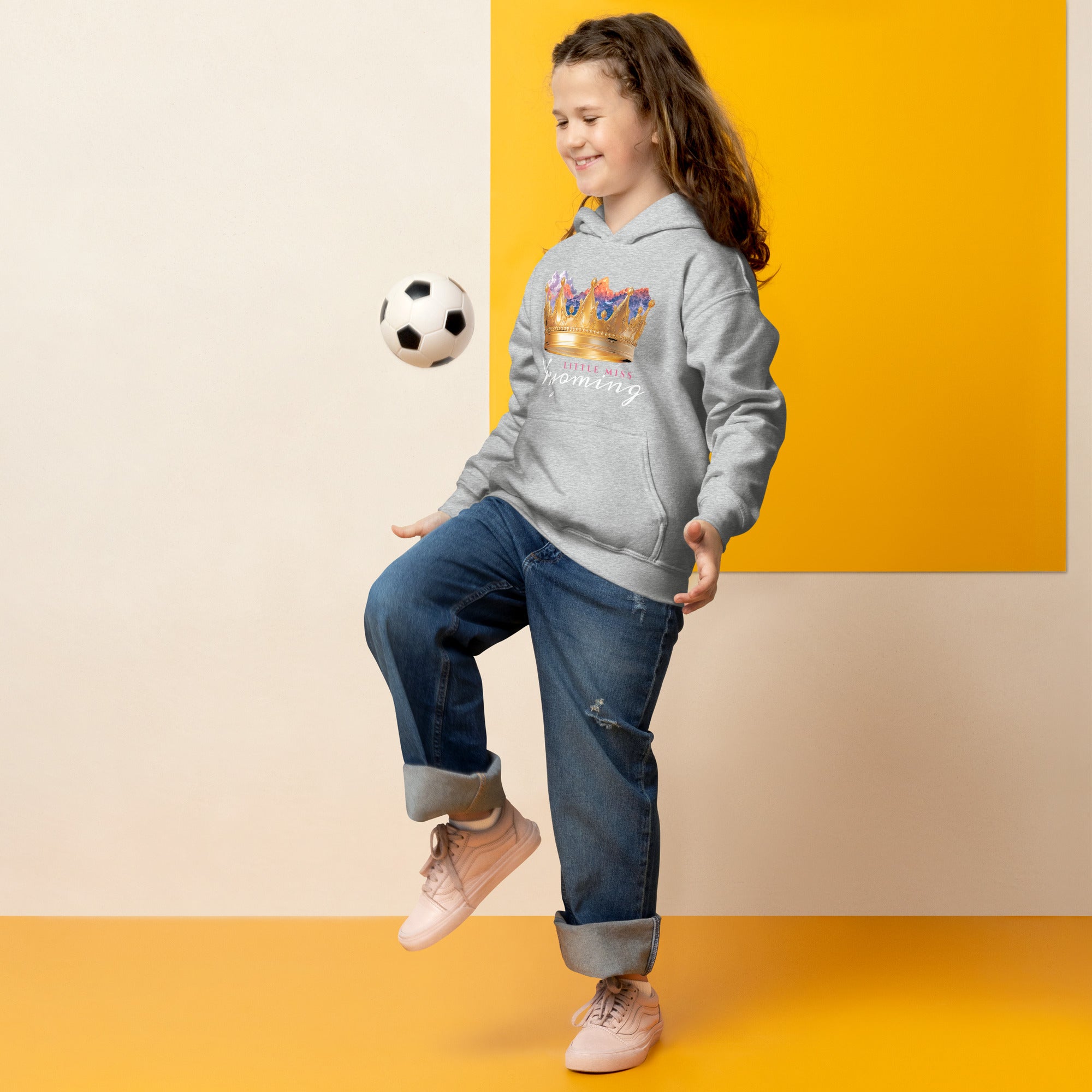 Child wearing a hoodie with a floral design, kicking a soccer ball against a yellow and beige background